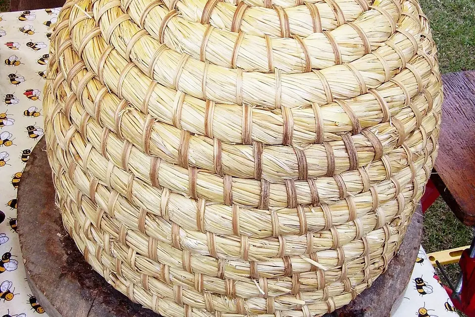 Ruche traditionnelle en forme de cloche, faite de boudins de paille tressés et cousus, posée sur un socle